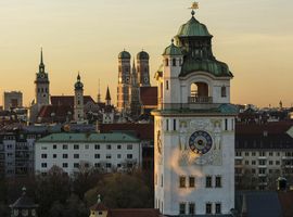 Überblick über die Dächer Münchens mit den verschiedenen Kirchtürmen im Sonnenuntergang.