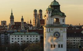 Überblick über die Dächer Münchens mit den verschiedenen Kirchtürmen im Sonnenuntergang.