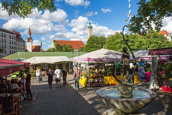 Menschen, die an einem sonnigen Tag die bunten Marktstände auf dem Münchner Viktualienmarkt durchstöbern