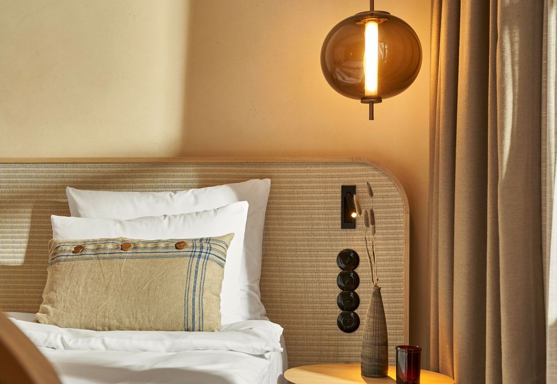 Ein natürliches Kissen mit Streifenmuster liegt vor geflochtenem Kopfteil mit Leselicht