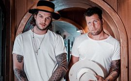 Gabriel Schütt and Patrick Köppchen stand next to each other and present one of their handmade hats