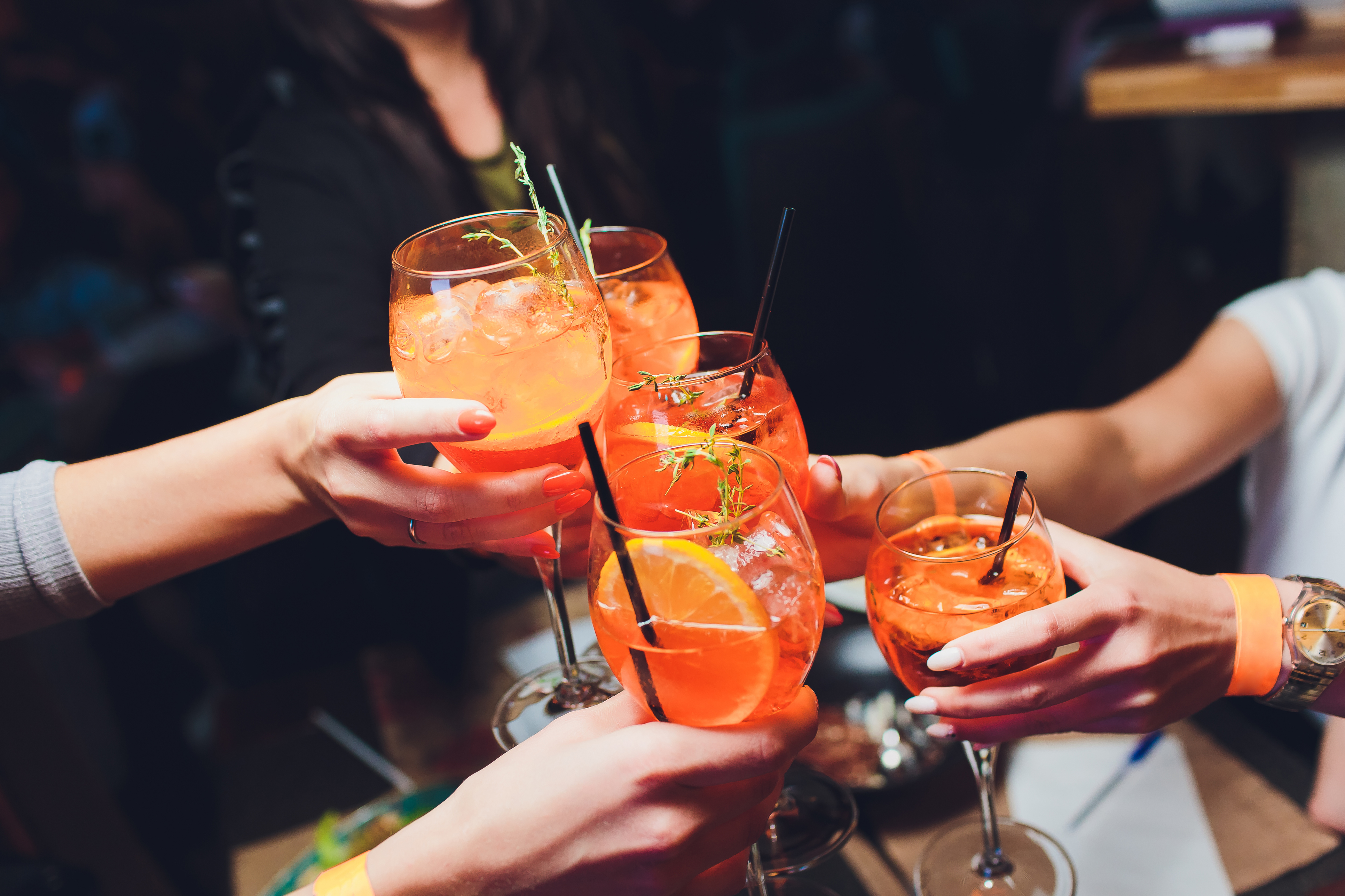 Mehrere Hände stoßen mit Aperol Spritz in lebendiger Bar-Atmosphäre an